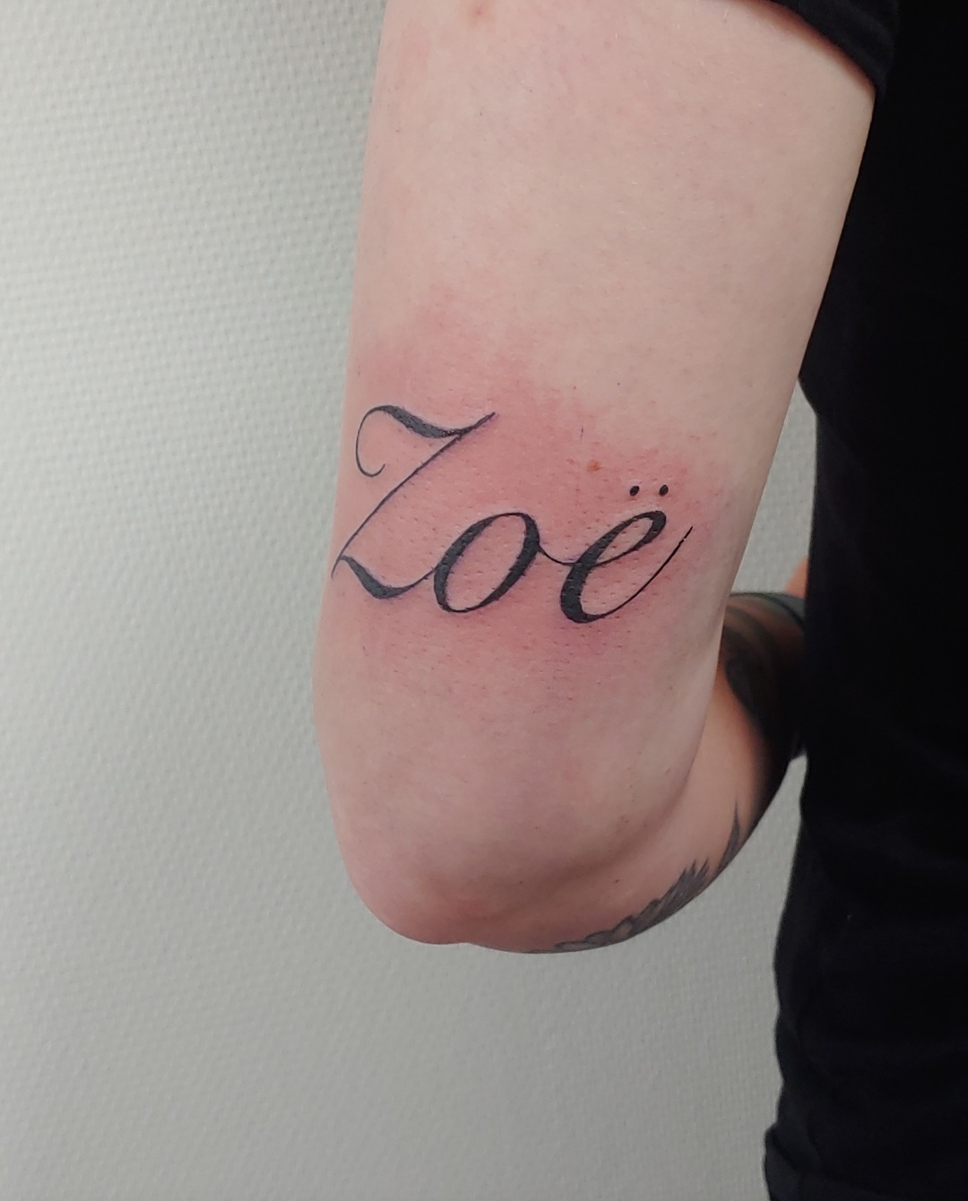 Tattoo met de naam Zoë in sierletters op een bovenarm